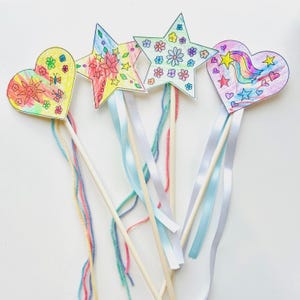 May include: Four colorful, handmade wands with star and heart-shaped toppers. Each wand features a wooden dowel, decorated with drawings of flowers, stars, and rainbows. Ribbons and yarn in various colors dangle from the wands, creating a whimsical effect.