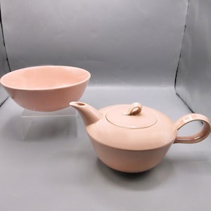 May include: A pink ceramic teapot and bowl set. The teapot has a lid and a handle. The bowl is round and has a wide rim.