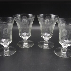 May include: Set of four clear glass stemmed drinking glasses with etched designs. The glasses have a wide bowl and a delicate stem.