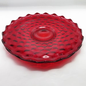 May include: A ruby red glass serving plate with a scalloped edge. The plate features a diamond pattern and a central, raised design. The plate is likely vintage and suitable for serving appetizers or desserts.