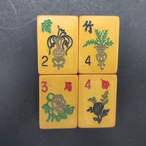 May include: Four rectangular yellow mahjong tiles arranged in a square grid. Each tile features engraved illustrations of plants or vases in black, green, and red ink, accompanied by the numerals 2, 3, 4, and 4, along with various Chinese characters.