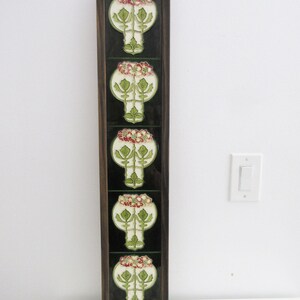 May include: A rectangular, framed wall art piece featuring five decorative tiles. Each tile displays a stylized floral design with white, green, and red accents against a black background. The frame is a dark brown color.