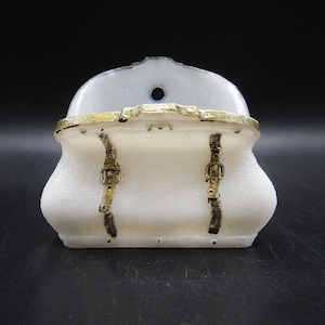 May include: White ceramic purse with gold trim and a textured surface. The purse has two gold buckles on the front.