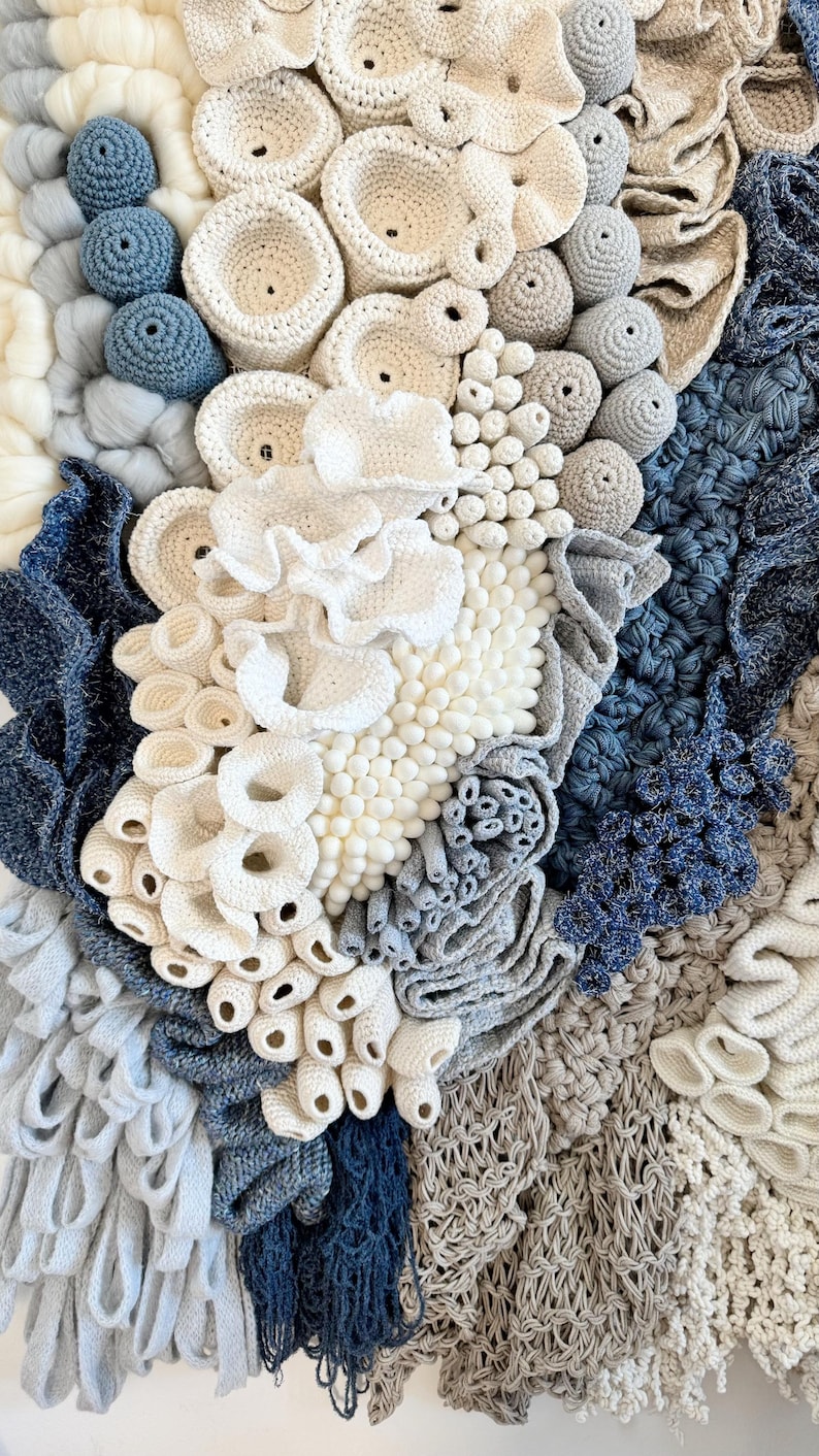 Puede incluir: Un tapiz de pared texturizado con elementos de ganchillo y tejido en tonos blancos, azules y grises. El dise&ntilde;o incorpora formas circulares y org&aacute;nicas, creando una obra de arte t&aacute;ctil y visualmente interesante.