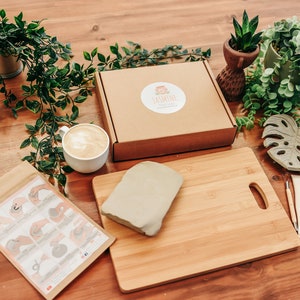 May include: A craft kit for making clay sculptures. The kit includes a block of clay, a wooden cutting board, a small container of glaze, four sculpting tools, a paper instruction sheet, and a monstera leaf mold.