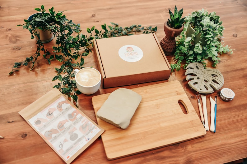 May include: A craft kit for making clay sculptures. The kit includes a block of clay, a wooden cutting board, a small container of glaze, four sculpting tools, a paper instruction sheet, and a monstera leaf mold.