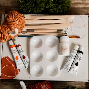 May include: A craft kit with a Highland cow figurine, paint tubes in orange and brown, a white paint palette, sealer, and tools. The kit includes a brush and instructions, all inside a box.