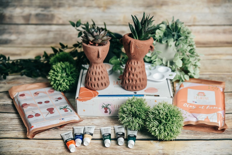 May include: A craft kit with two terracotta face planter pots, green plants, paint tubes, and a paint palette. The kit includes instructions for painting the planters.