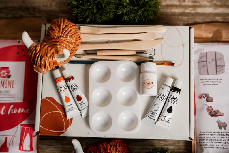 May include: A craft kit with a Highland cow figurine, paint tubes in orange and burnt sienna, a white paint palette, sealer, and tools. The kit includes instructions and is designed for creative projects.