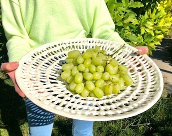 Puede incluir: Un plato de servir de cerámica blanca con un diseño decorativo de calado. El plato está lleno de un racimo de uvas verdes.