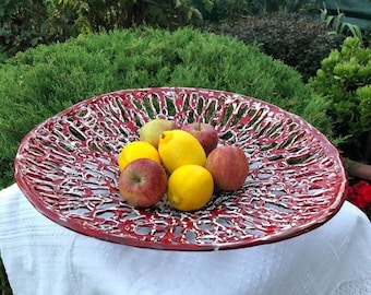 Puede incluir: Un cuenco de fruta de cerámica roja con un esmalte blanco y un diseño único e intrincado. El cuenco está lleno de manzanas y limones.