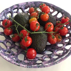 Pode incluir: Uma tigela de cerâmica roxa com um design de treliça contém uma variedade de tomates vermelhos e duas abacates. A tigela tem um esmalte salpicado.