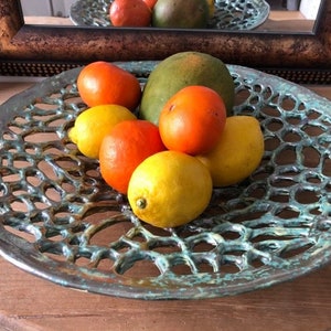 Puede incluir: Un cuenco de fruta de cerámica verde con un diseño de celosía. El cuenco está lleno de limones, naranjas y un mango verde.