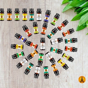 May include: A selection of essential oil bottles arranged in a circle on a wooden surface. The bottles are labelled with different names, including "Anxiety".