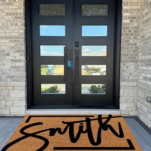 May include: A brown coir doormat with a black border and the word "Smith" written in a cursive font.