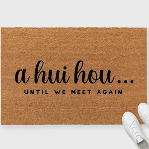 May include: A brown coir doormat with the text "a hui hou... until we meet again" in black cursive lettering.