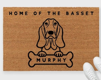 May include: A brown doormat with the text "Home of the Basset" and a black and white illustration of a Basset Hound holding a bone with the name "Murphy" on it.