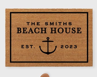 May include: A brown coir doormat with a black border and the text "THE SMITHS BEACH HOUSE EST. 2023" with an anchor symbol in between the words "EST." and "2023".
