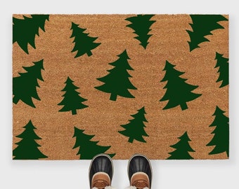 May include: A brown doormat with a green Christmas tree pattern. The doormat is made of coir and has a textured surface. Two brown and black winter boots are placed on the doormat.