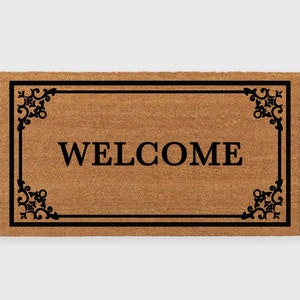 May include: A brown coir doormat with a black border and ornate corner designs. The word "WELCOME" is printed in black letters in the center of the mat.