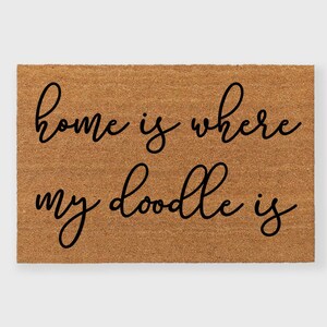 May include: A brown coir doormat with the text "home is where my doodle is" written in black cursive font.