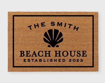 May include: A brown doormat with black text and a seashell graphic. The text reads "The Smith Beach House Established 2023".