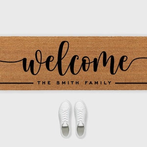 May include: A brown coir doormat with the text "welcome" in a black cursive font. Below the text is a black line with the text "the smith family".