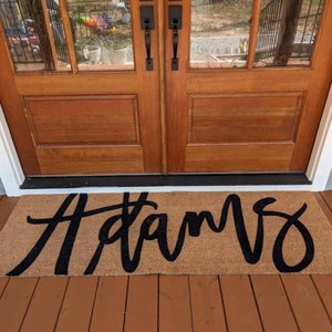May include: A brown doormat with the word "Adams" written in black cursive lettering.