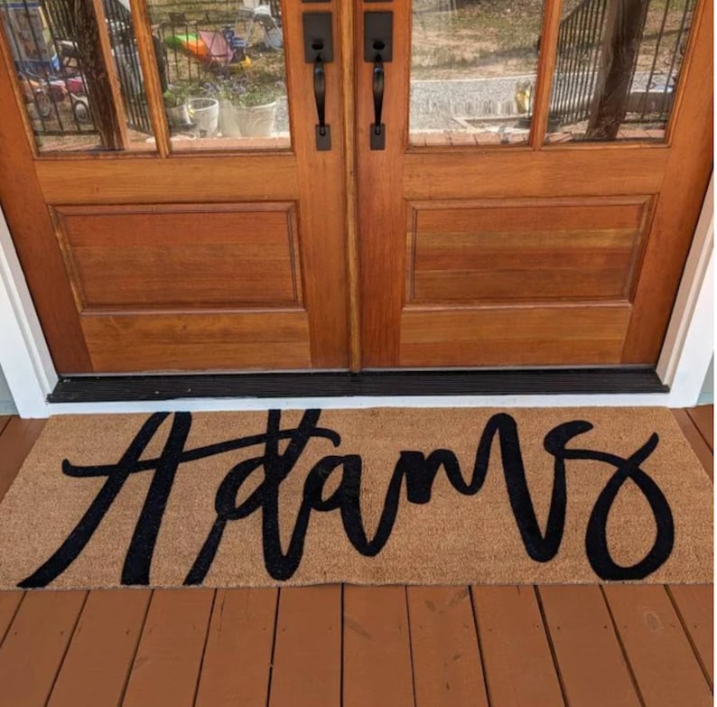 May include: A brown doormat with the word "Adams" written in black cursive lettering.