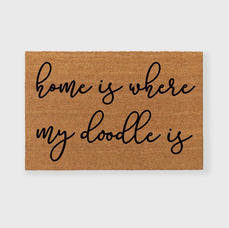 May include: A brown coir doormat with the text "home is where my doodle is" written in black cursive font.