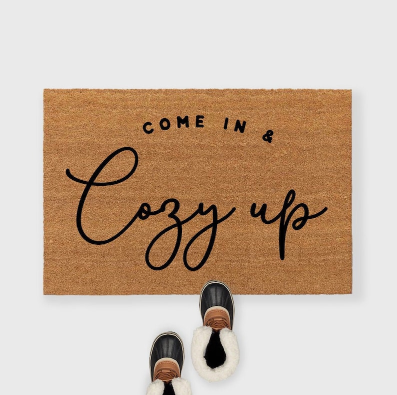 May include: A brown coir doormat with the text "Come in & Cozy up" in black script font.