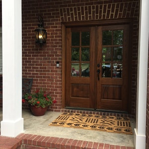 May include: A brown door with glass panels and a black doormat with a geometric pattern in front of a brick house.