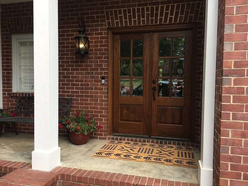May include: A brown door with glass panels and a black doormat with a geometric pattern in front of a brick house.