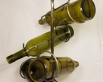 Pode incluir: Um suporte de garrafa de vinho de metal com uma parte superior decorativa de metal torcido. O suporte tem capacidade para quatro garrafas de vinho.