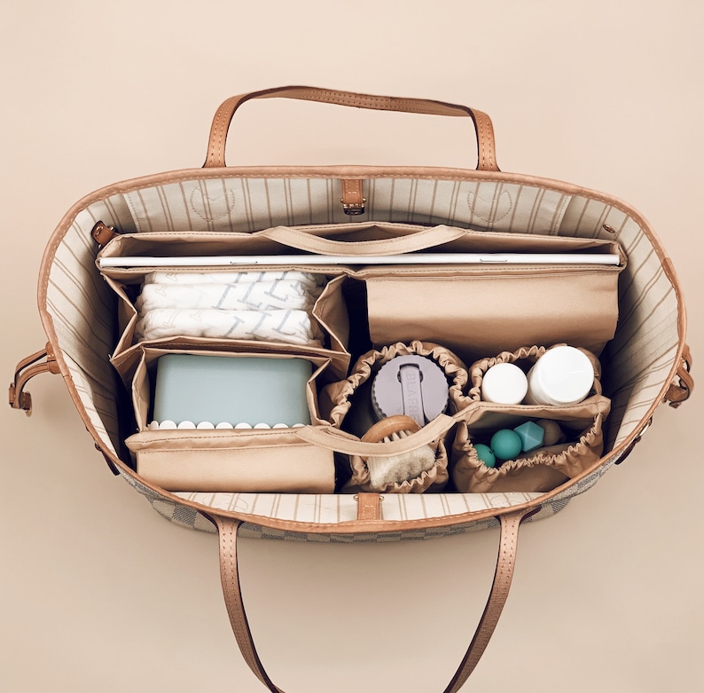 May include: A brown and tan patterned tote bag with a zippered top and multiple compartments. The bag is filled with various items, including a laptop, a water bottle, a small container, and a few other items.