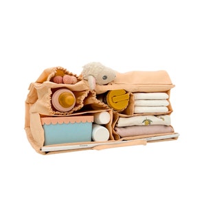 May include: A beige diaper bag organizer with multiple compartments, filled with baby essentials like bottles, a stuffed animal, and clothing.