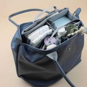 May include: A blue tote bag with multiple compartments and pockets, filled with baby supplies, including diapers, wipes, a bottle, and a pacifier.