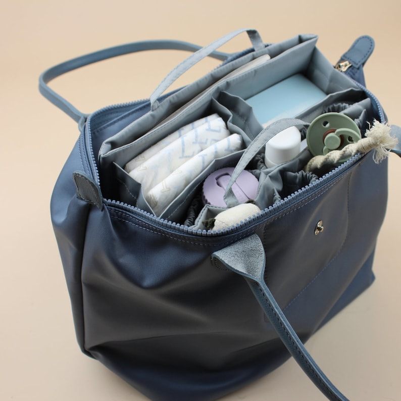 May include: A blue tote bag with multiple compartments and pockets, filled with baby supplies, including diapers, wipes, a bottle, and a pacifier.