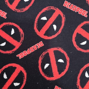 May include: A black fabric featuring a repeating pattern of the red Deadpool logo, which consists of a red circle with a diagonal slash and two white eye shapes. The word DEADPOOL is printed in red capital letters throughout the fabric design.