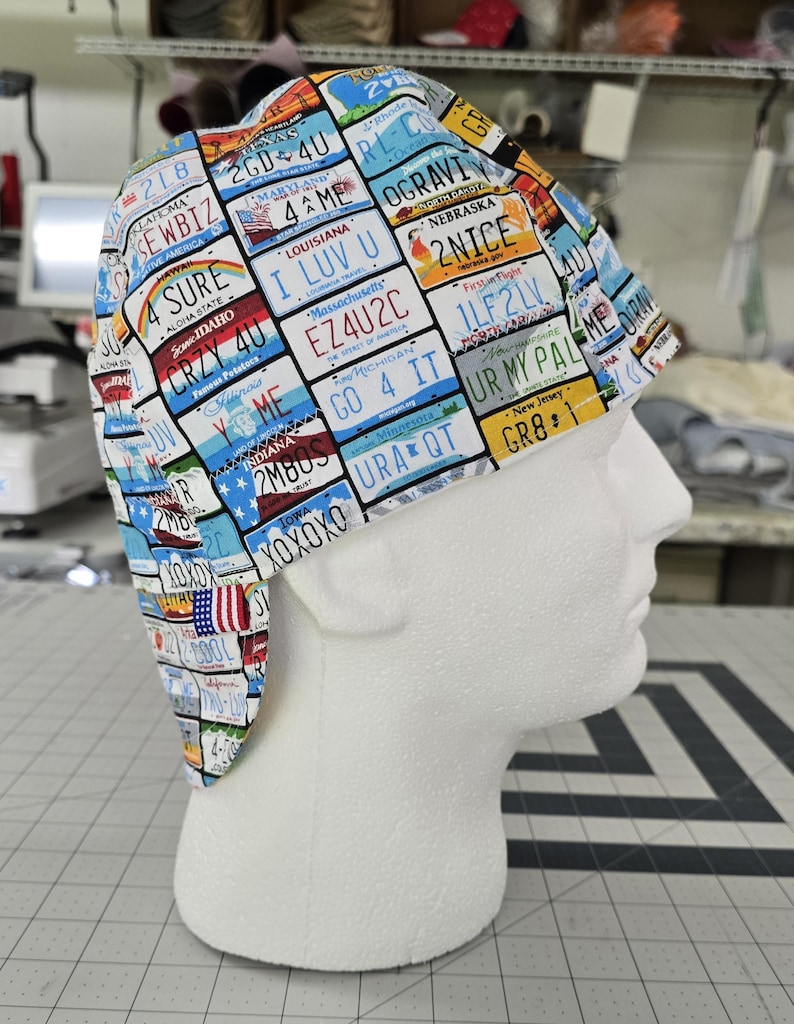 May include: A scrub cap featuring a colorful all-over print of various United States license plates. The fabric displays multiple state names and alphanumeric combinations such as 2GD 4U, I LUV U, EZ4U2C, 2NICE, 1LF2LV, UR MY PAL, GO 4 IT, and XOXOXO.