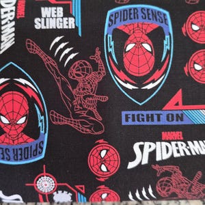 May include: Black fabric featuring a repeating pattern of Spider-Man graphics, including red and black character masks, full-body action poses, and blue shield emblems. Text includes Spider Sense, Web Slinger, Fight On, and Marvel Spider-Man.