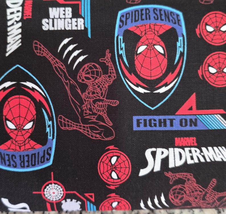 May include: Black fabric featuring a repeating pattern of Spider-Man graphics, including red and black character masks, full-body action poses, and blue shield emblems. Text includes Spider Sense, Web Slinger, Fight On, and Marvel Spider-Man.