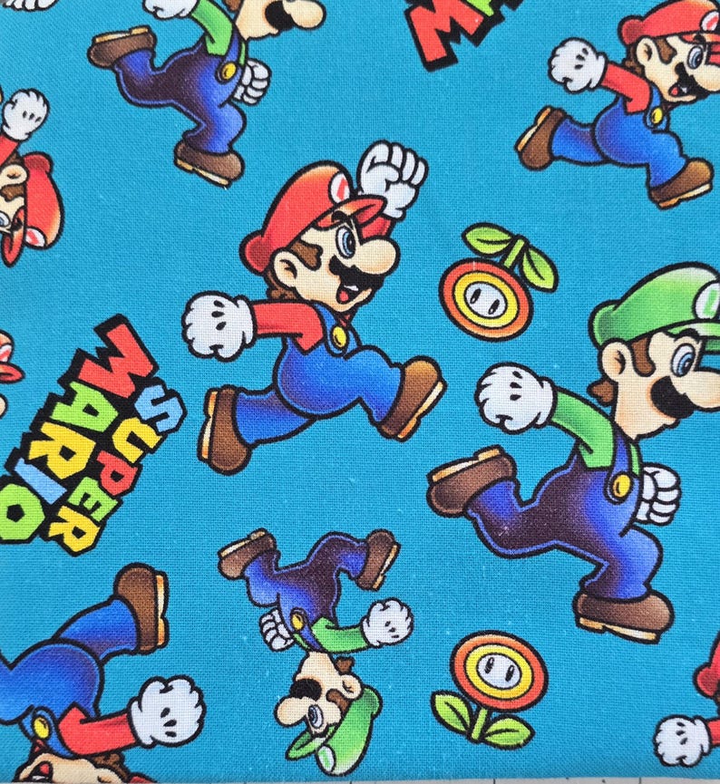 May include: A bright blue fabric featuring a repeating pattern of Mario and Luigi characters in their signature red and green outfits, along with orange fire flower icons and the text Super Mario printed in bold black and yellow letters.