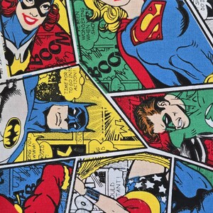 May include: A fabric print featuring a collage of DC comic book panels with characters including Batgirl, Supergirl, Batman, Green Lantern, The Flash, and Wonder Woman. The design uses vibrant primary colors and includes speech bubbles with text.