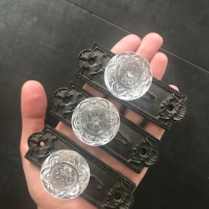 May include: Three antique-style door knobs with clear glass accents and ornate metal plates. The knobs have a decorative floral design.