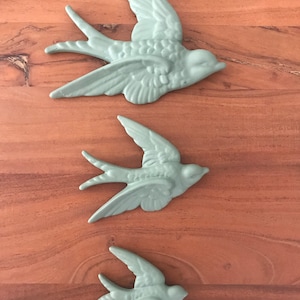 Peut inclure: Trois hirondelles en céramique de différentes tailles, toutes peintes dans un vert sauge mat. Les hirondelles sont en vol, les ailes déployées.