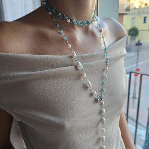 Puede incluir: Un collar de varias capas con perlas de agua dulce y cuentas de color turquesa. El collar tiene un diseño largo y drapeado con un cierre plateado. La capa superior es de estilo gargantilla, mientras que la capa inferior se extiende por el pecho.