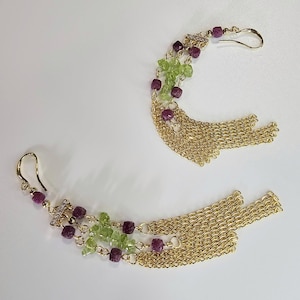 Puede incluir: Un par de pendientes dorados con un diseño en cascada. Cada pendiente presenta un gancho, una fila de pequeñas cuentas cuadradas de color rojo oscuro y una fila de cuentas de color verde claro. Cadenas doradas cuelgan de la parte inferior.