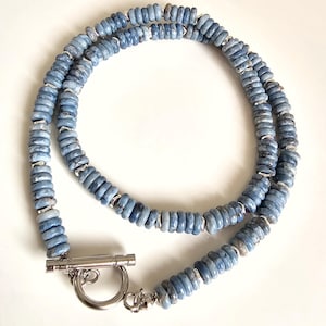 Puede incluir: Un collar de cuentas azules con cierre plateado. El collar está hecho de pequeñas cuentas redondas azules con espaciadores plateados. El cierre es un cierre de palanca plateado.