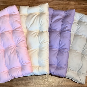 May include: Four tufted floor cushions in different colours: pink, white, lavender, and light blue. The cushions are rectangular and have a quilted design.